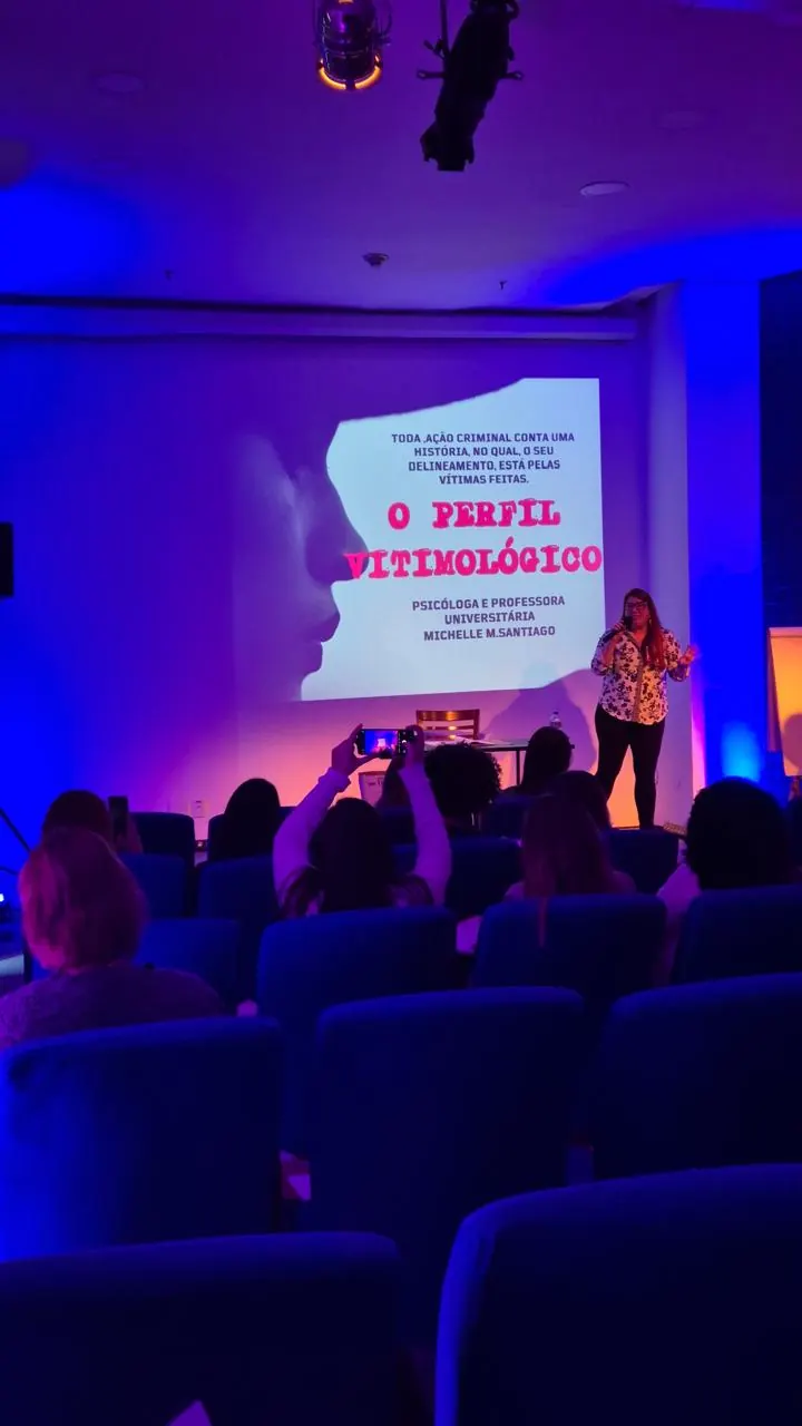 Plateia diante do telão com o título O perfil vitimológico, com Michelle Santiago no palco